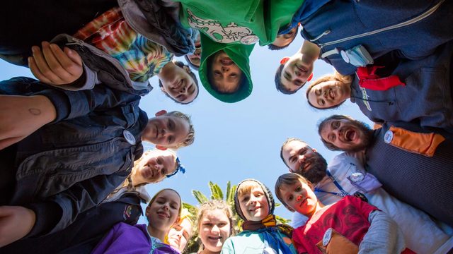 Campers and a leader huddled in a circle, smiling down at the camera
