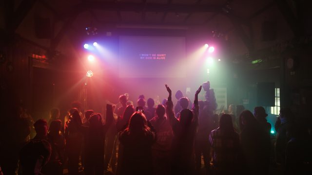 Campers with hands raised during worship under coloured lights